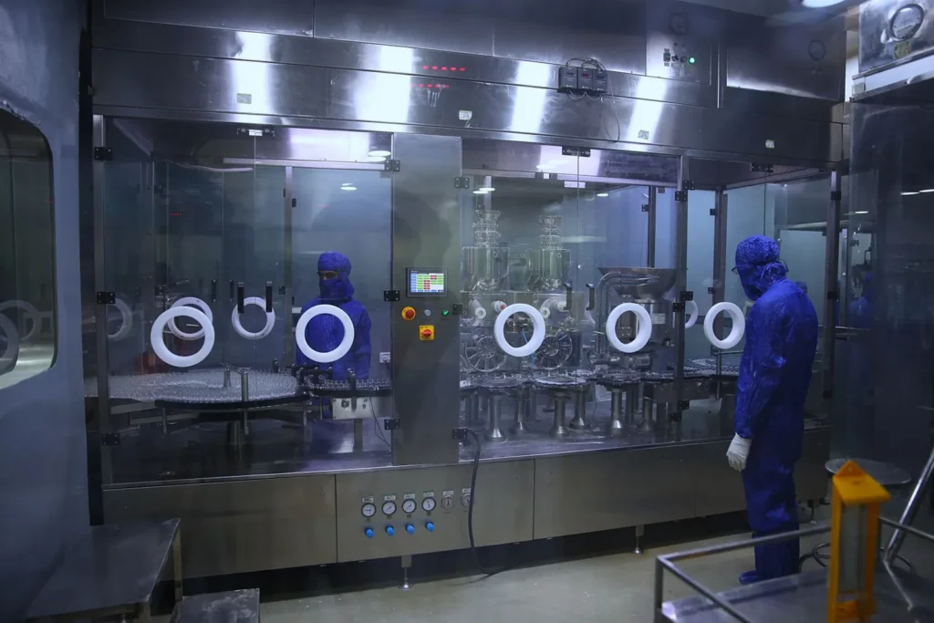 Operator in protective coveralls working beside a sterile filling line inside a pharmaceutical manufacturing cleanroom