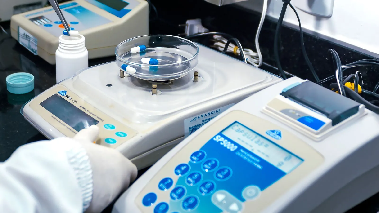 Pharmaceutical quality control testing Gloved hand weighing pharmaceutical capsules on an analytical balance in a quality control laboratory