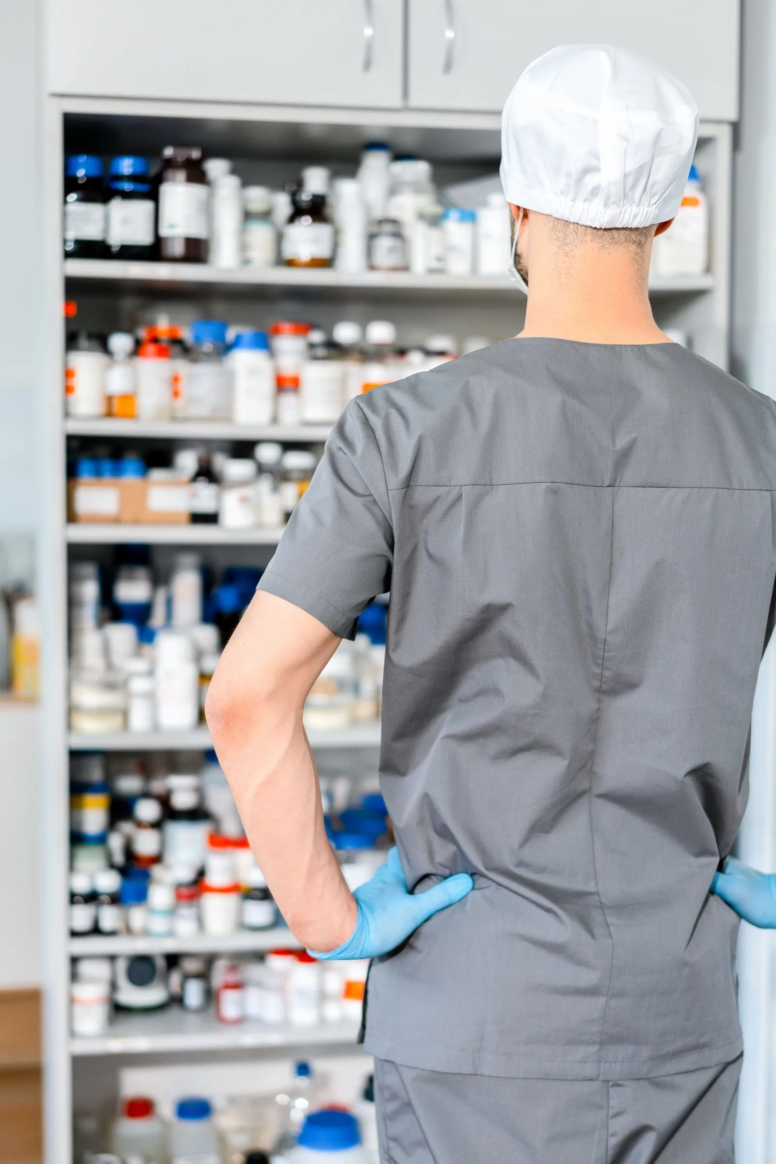 Post-market oversight at the point of dispensing Pharmacist in scrubs and surgical cap arranging medicine stock on pharmacy dispensary shelves