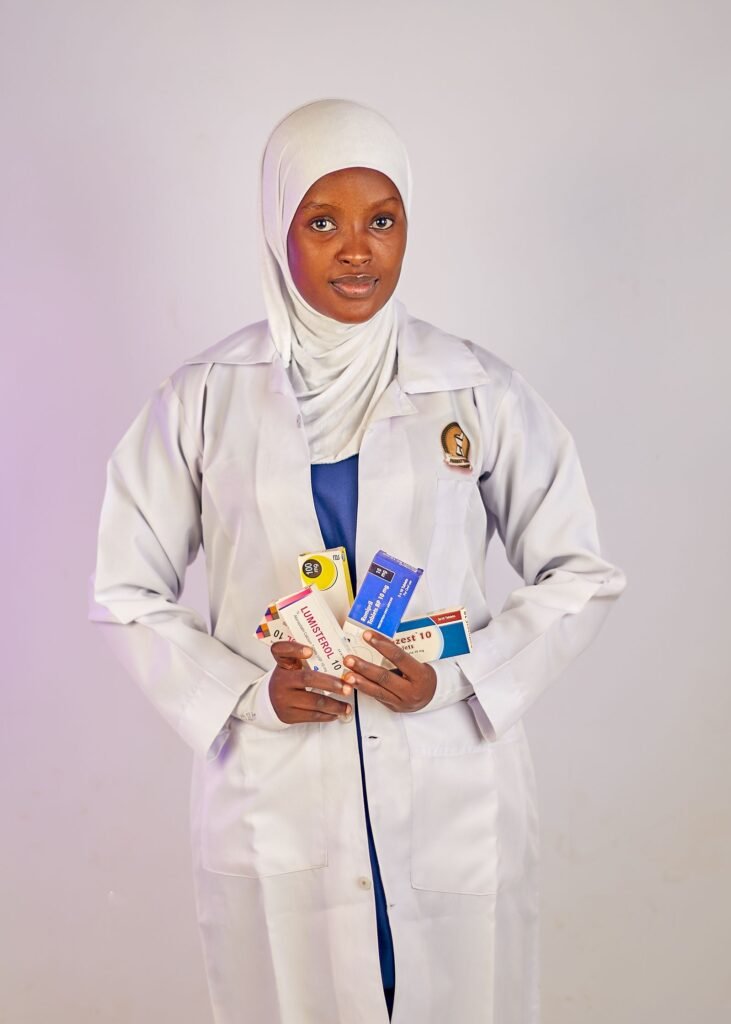 Pharmacist in a white coat and hijab holding several boxed medicines in a studio portrait